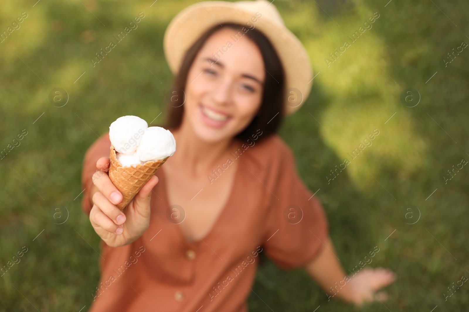 Photo of Happy young woman with delicious ice cream in waffle cone outdoors, focus on hand