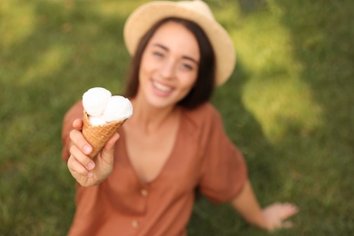 Photo of Happy young woman with delicious ice cream in waffle cone outdoors, focus on hand