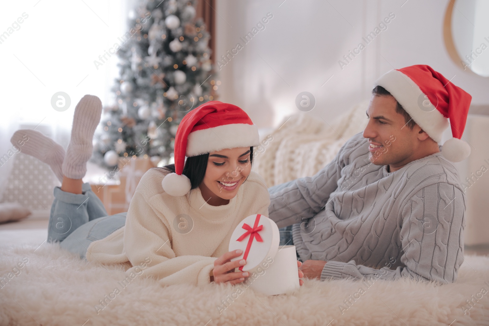 Photo of Couple opening gift box in room with Christmas tree