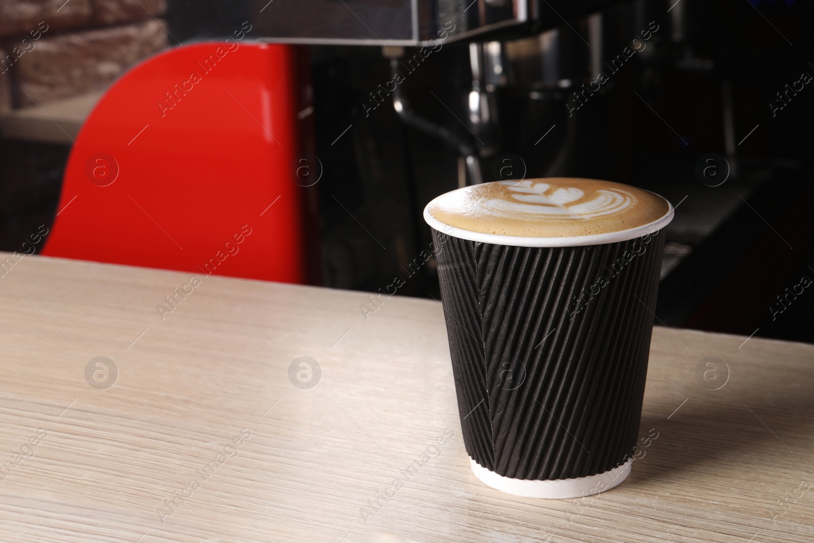 Photo of Takeaway paper cup of fresh aromatic coffee on wooden counter in cafe, space for text