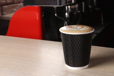 Photo of Takeaway paper cup of fresh aromatic coffee on wooden counter in cafe, space for text