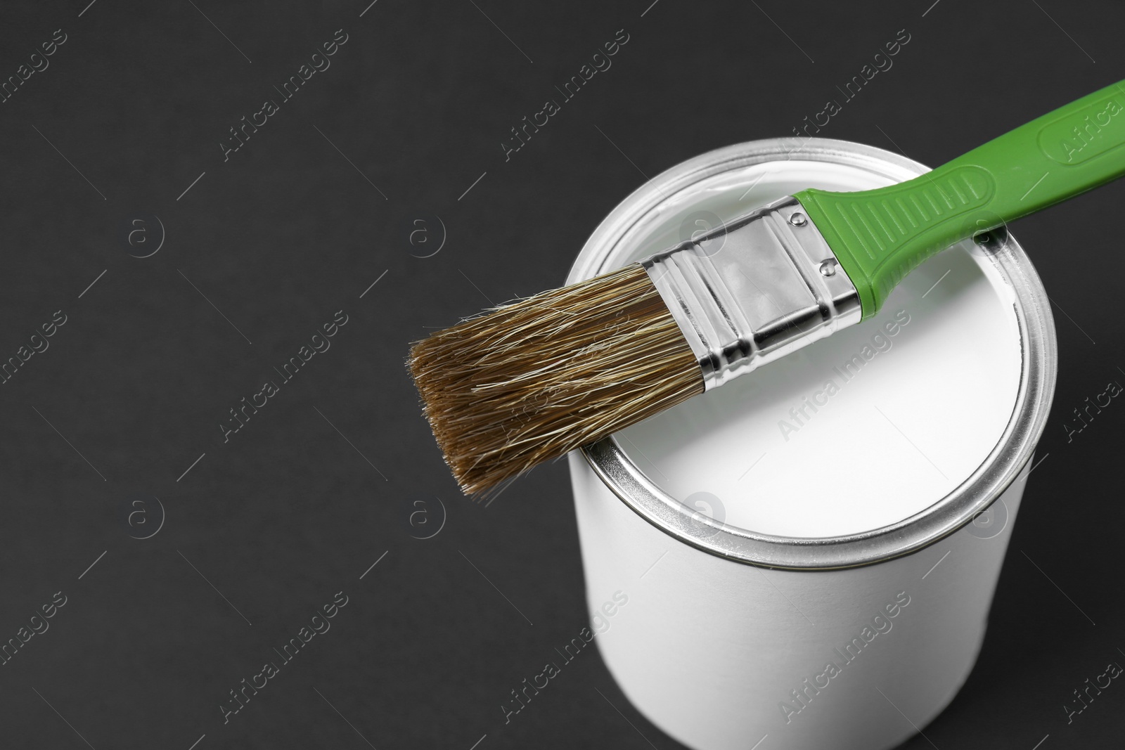 Photo of Can of white paint with brush on black background, closeup. Space for text