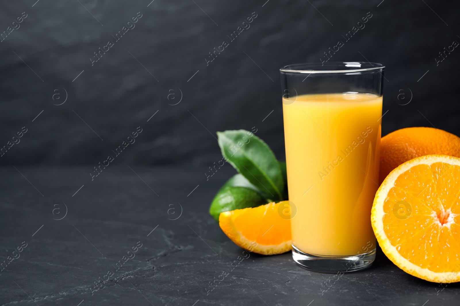 Photo of Glass of orange juice and fresh fruits on grey table. Space for text