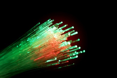 Optical fiber strands transmitting green and red light on black background, macro view