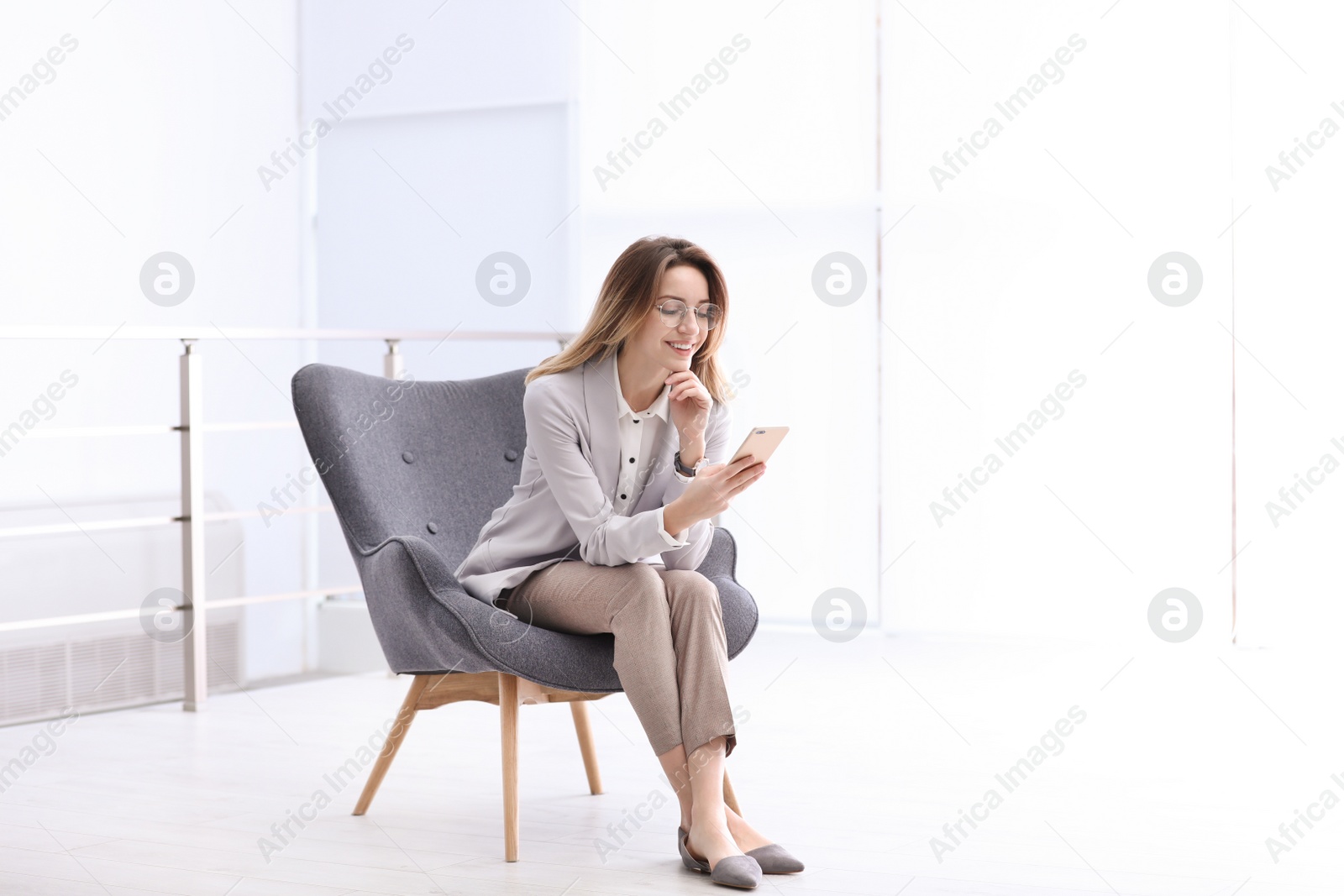 Photo of Young businesswoman with modern phone sitting in armchair indoors. Space for text
