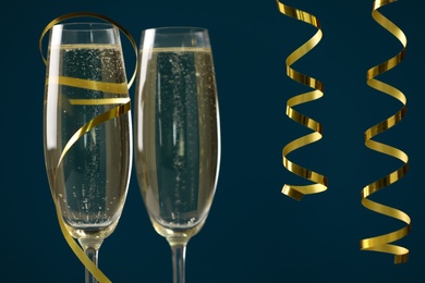 Photo of Glasses of champagne and serpentine streamers on dark blue background, closeup
