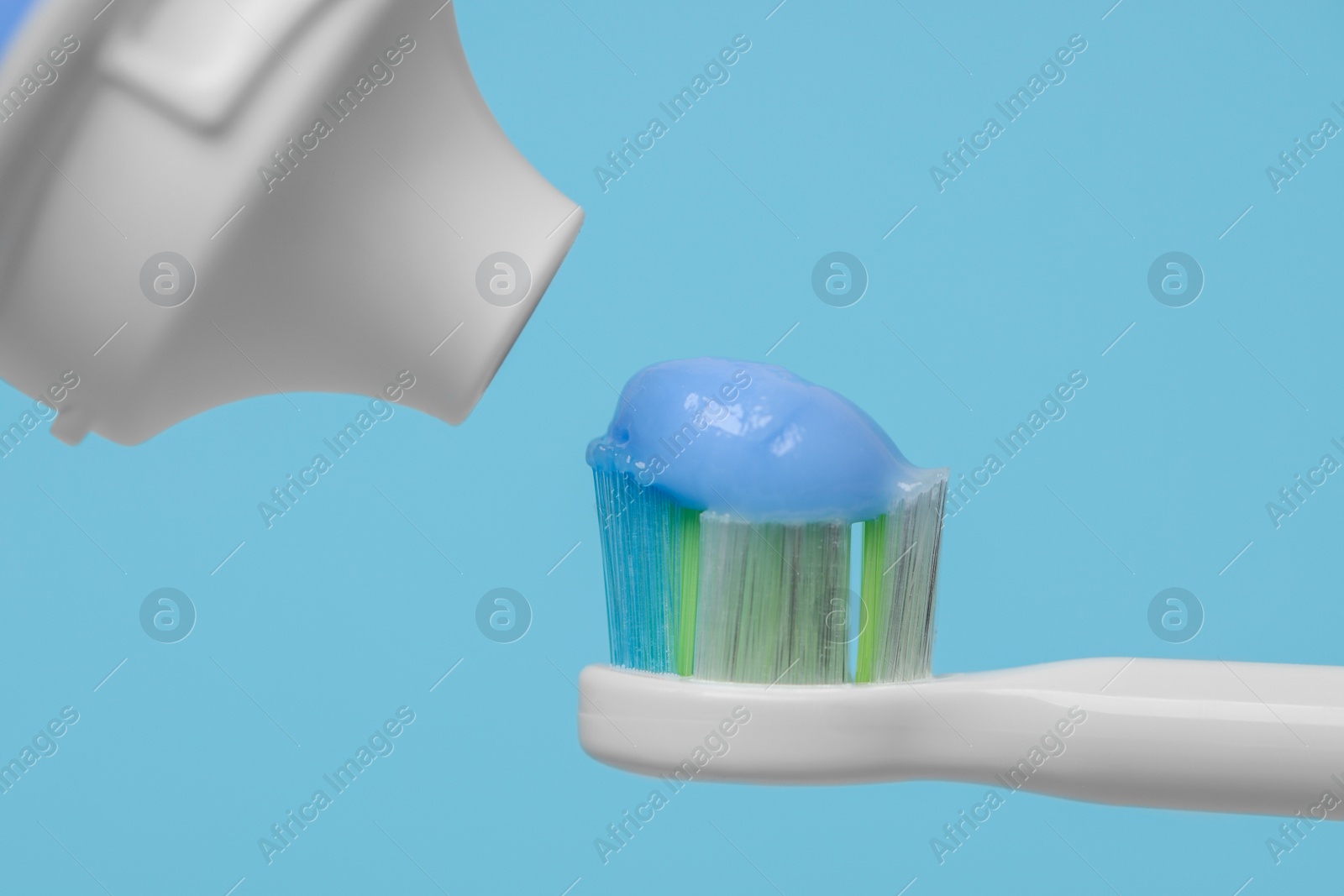 Photo of Electric toothbrush with paste on light blue background, closeup