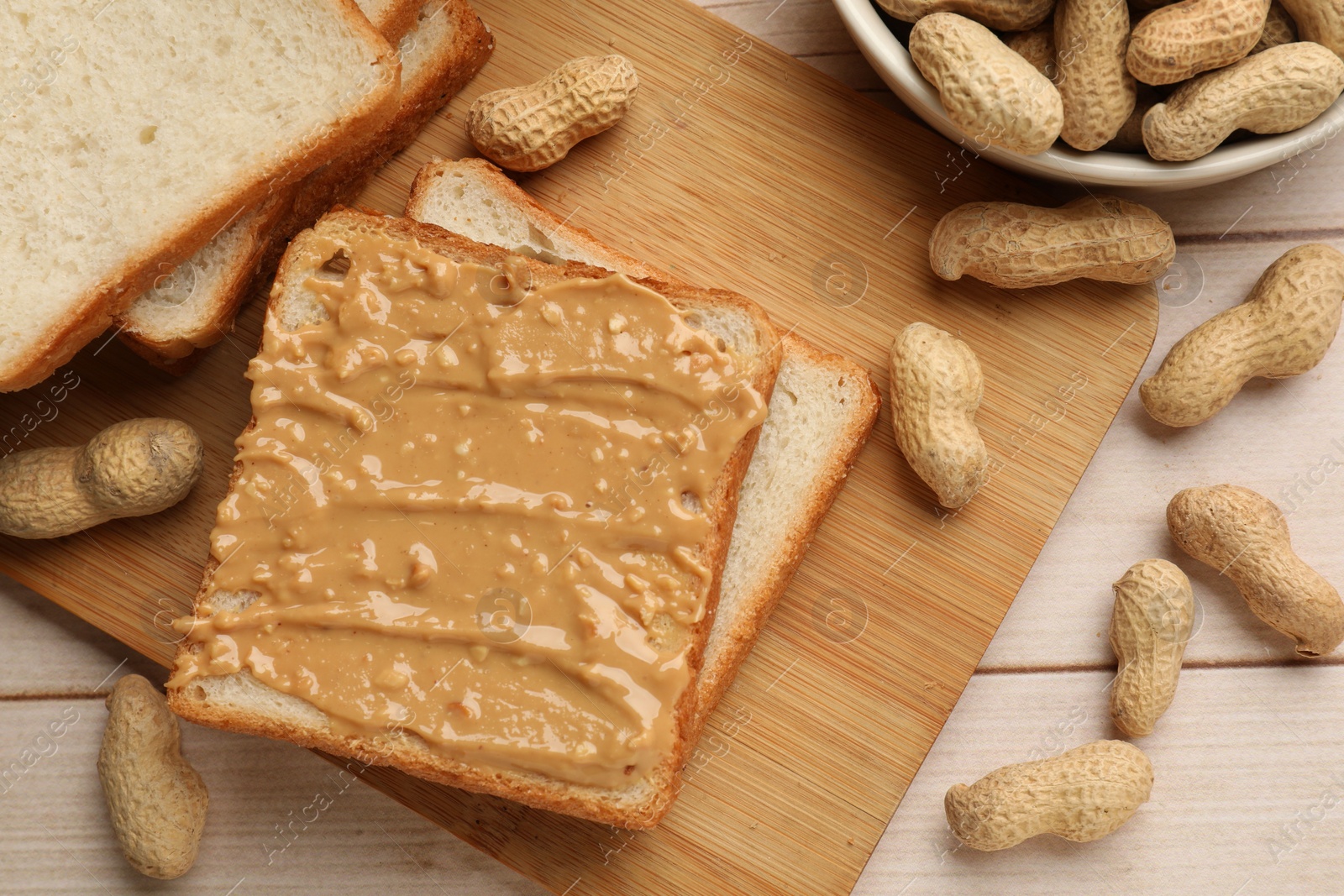 Photo of Delicious toasts with peanut butter and nuts on light wooden table, flat lay