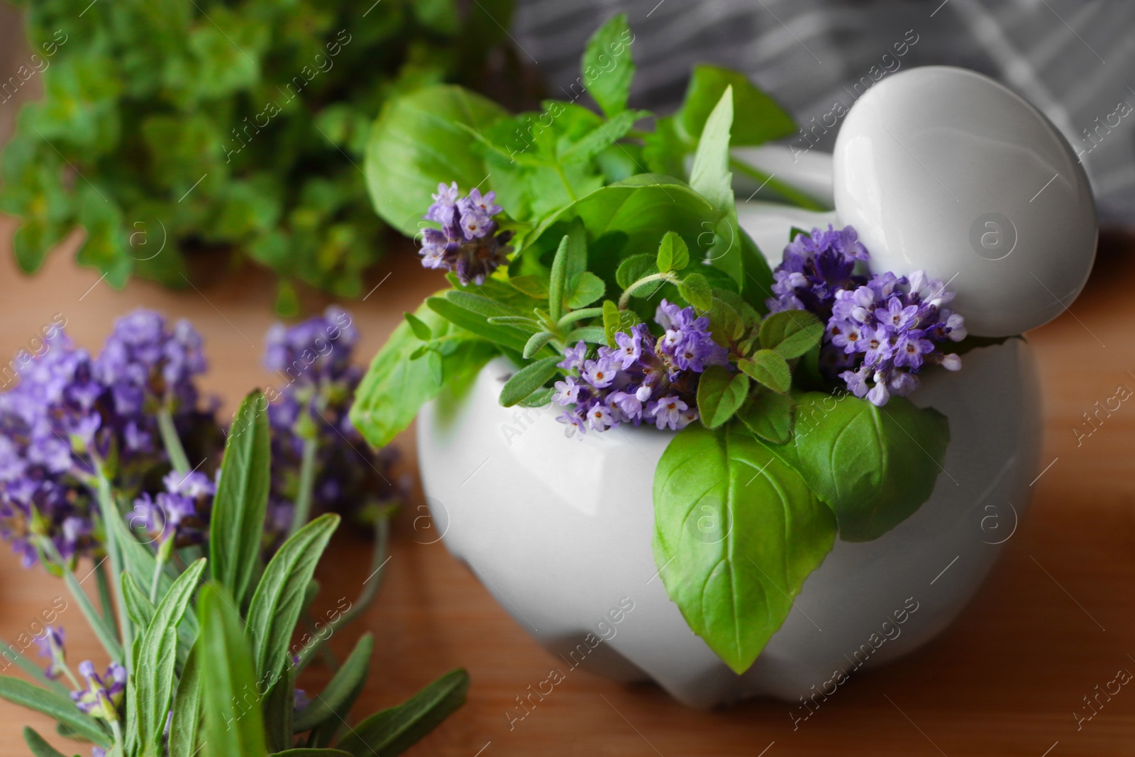 Photo of Mortar with fresh lavender flowers, herbs and pestle on wooden table, closeup