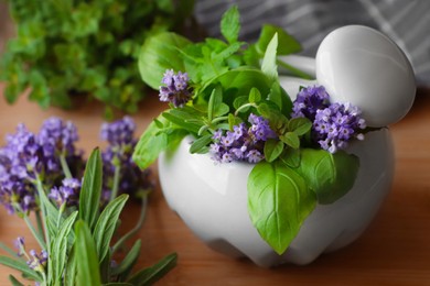 Mortar with fresh lavender flowers, herbs and pestle on wooden table, closeup