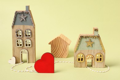 Photo of Decorative hearts and cord between two house models on pale yellow background symbolizing connection in long-distance relationship