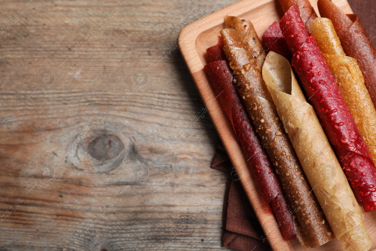 Photo of Delicious fruit leather rolls on wooden table, top view. Space for text