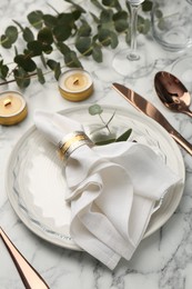 Beautiful place setting with candles and eucalyptus on white marble table