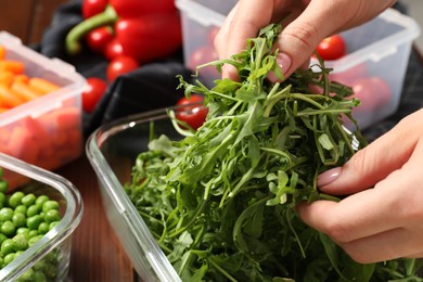 Photo of Woman putting arugula into glass container at table, closeup. Food storage