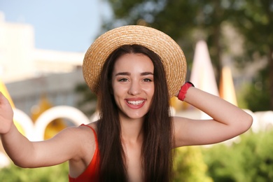 Photo of Happy young woman in stylish hat taking selfie outdoors on sunny day