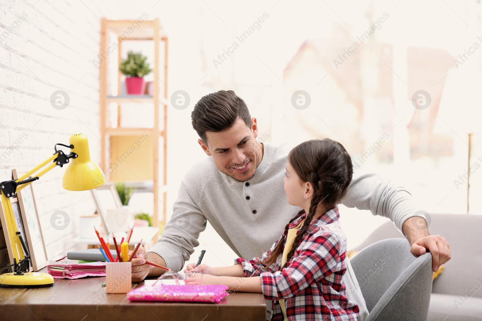 Photo of Man helping his daughter with homework at table indoors