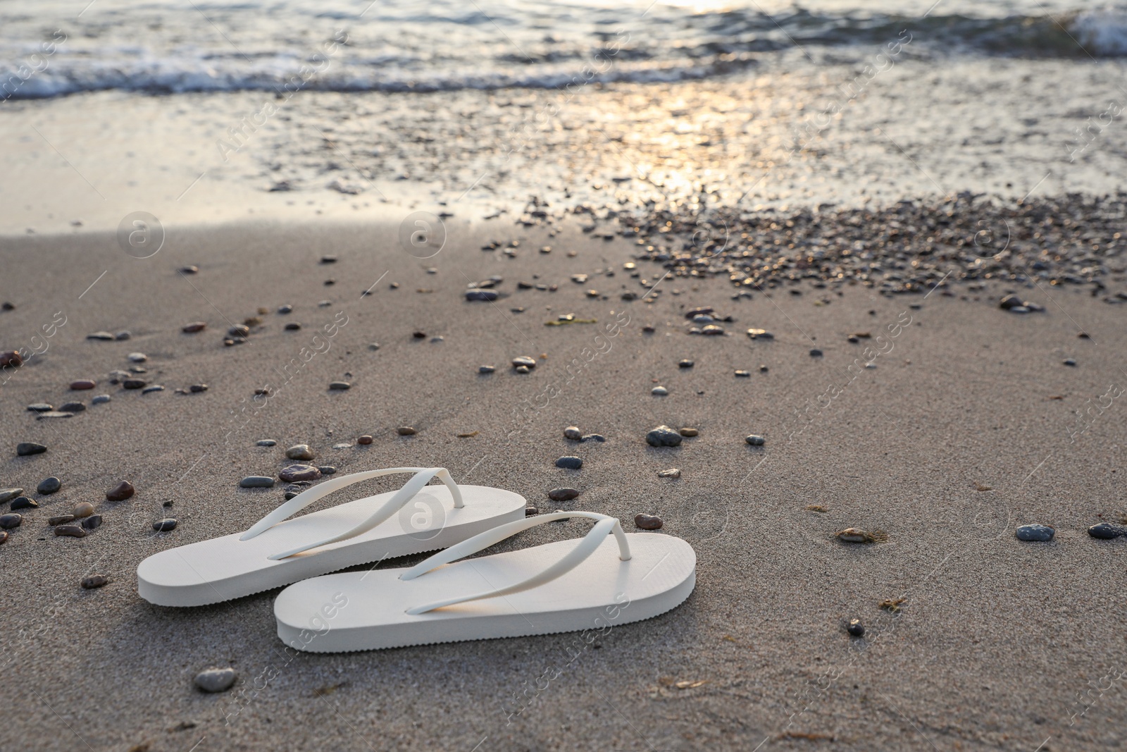 Photo of Stylish white flip flops on sand near sea. Space for text