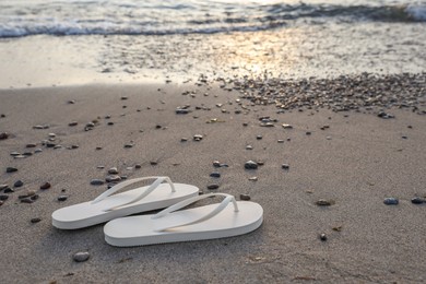 Stylish white flip flops on sand near sea. Space for text