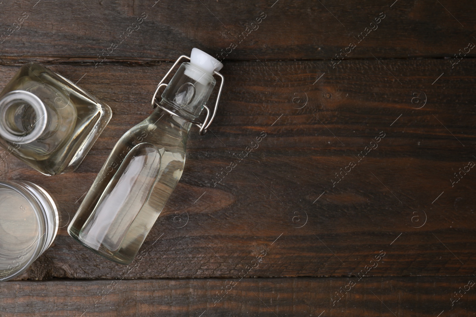 Photo of Vinegar in bottles and glass on wooden table, flat lay. Space for text