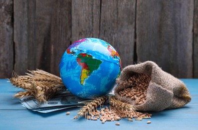 Photo of Globe and bag of wheat grains on light blue wooden table. Import and export concept