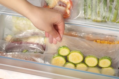 Photo of Woman putting vacuum bag with zucchini into fridge, closeup. Food storage