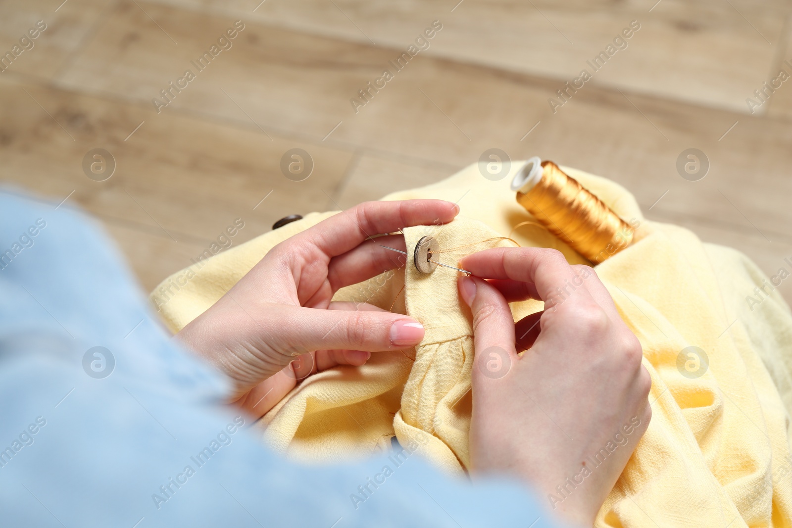 Photo of Woman sewing button with needle and thread onto shirt at home, closeup