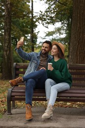 Happy young couple taking selfie on wooden bench in autumn park