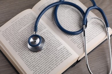 Photo of Open book and stethoscope on wooden table, closeup. Medical education