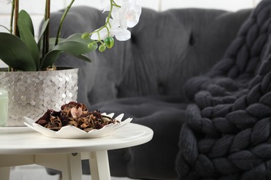 Aromatic potpourri of dried flowers in plate and beautiful houseplant on white table indoors. Space for text