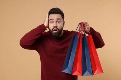 Shocked man with many paper shopping bags on beige background