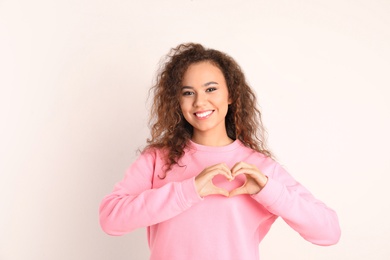 Photo of African-American woman making heart with her hands on white background