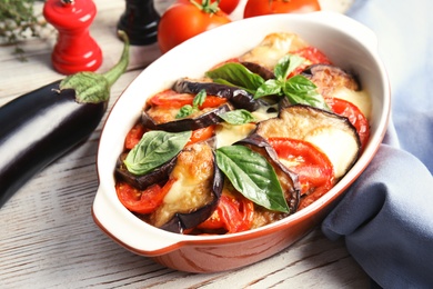 Photo of Baked eggplant with tomatoes, cheese and basil in dishware on table, closeup