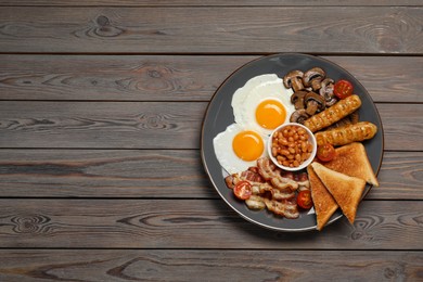 Plate of fried eggs, mushrooms, beans, tomatoes, bacon, sausages and toasts on wooden table, top view with space for text. Traditional English breakfast