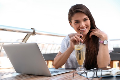 Photo of Beautiful woman with refreshing drink and laptop at outdoor cafe
