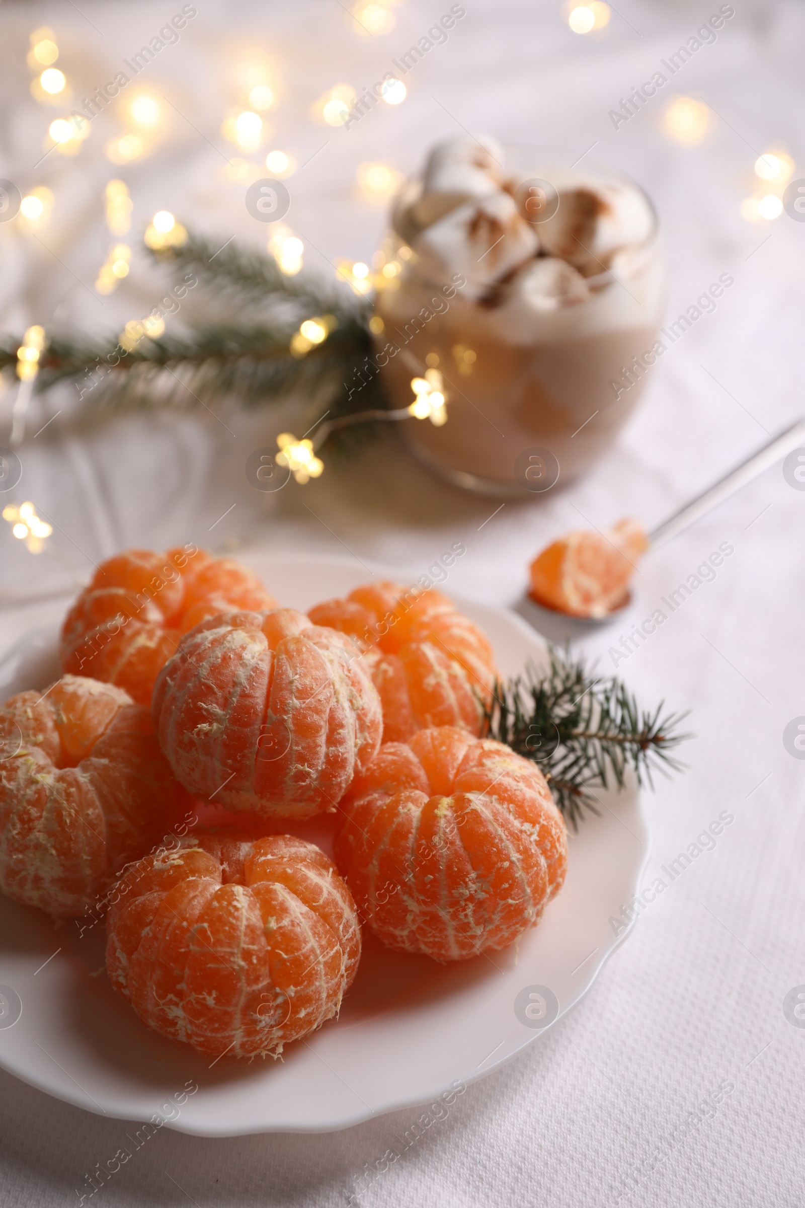 Photo of Peeled delicious ripe tangerines and glass of drink with marshmallows on white bedsheet