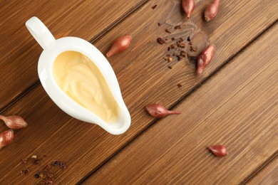 Photo of Tasty sauce in gravy boat, small onion bulbs and spice on wooden table, flat lay. Space for text