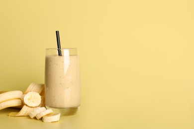 Photo of Glass of tasty smoothie with straw and cut banana on pale yellow background. Space for text