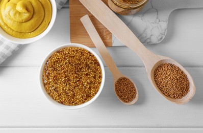 Bowls and spoons of whole grain mustard with seeds on white wooden table, flat lay