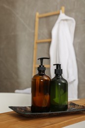 Wooden bath tray with bottles of shower gels on tub indoors, space for text