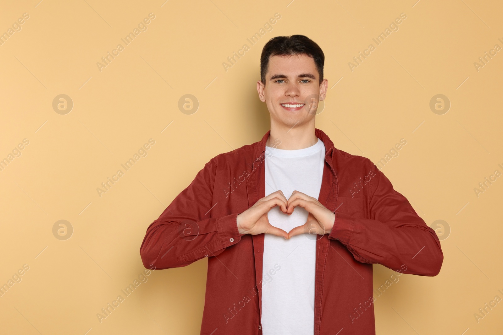 Photo of Happy volunteer making heart with his hands on beige background. Space for text