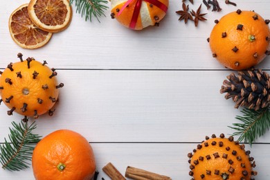 Pomander balls made of tangerines with cloves, spices and fir branches on white wooden table, flat lay. Space for text