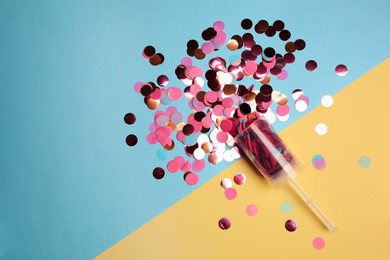 Party popper with pink confetti on color background, flat lay. Space for text