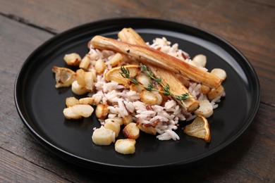 Photo of Plate with baked salsify roots, lemon and rice on wooden table, closeup