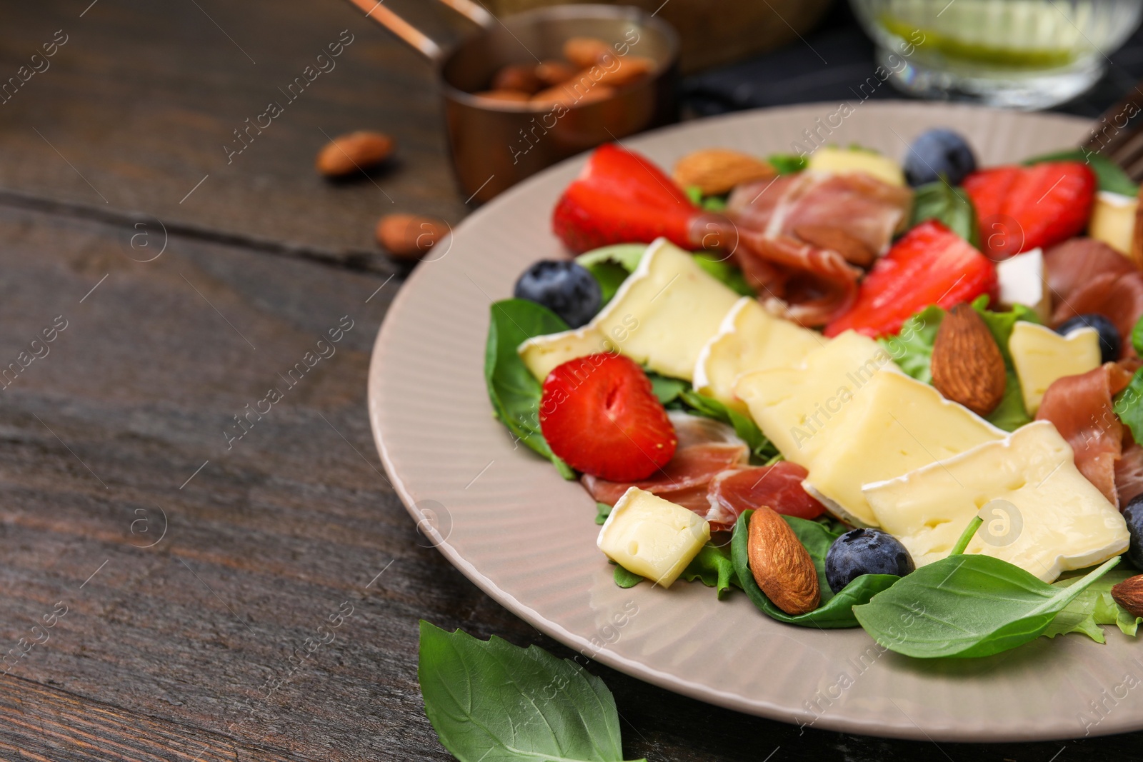 Photo of Tasty salad with brie cheese, prosciutto, almonds and berries on wooden table, closeup. Space for text