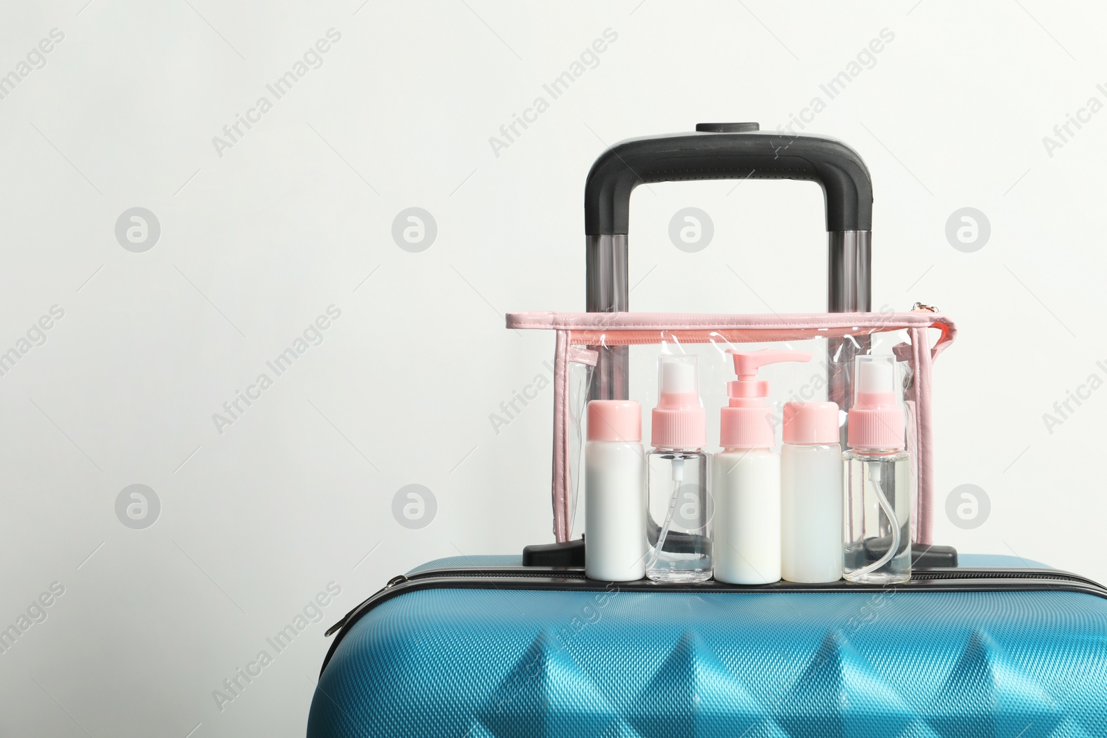 Photo of Cosmetic travel kit in plastic bag on suitcase against light background, space for text