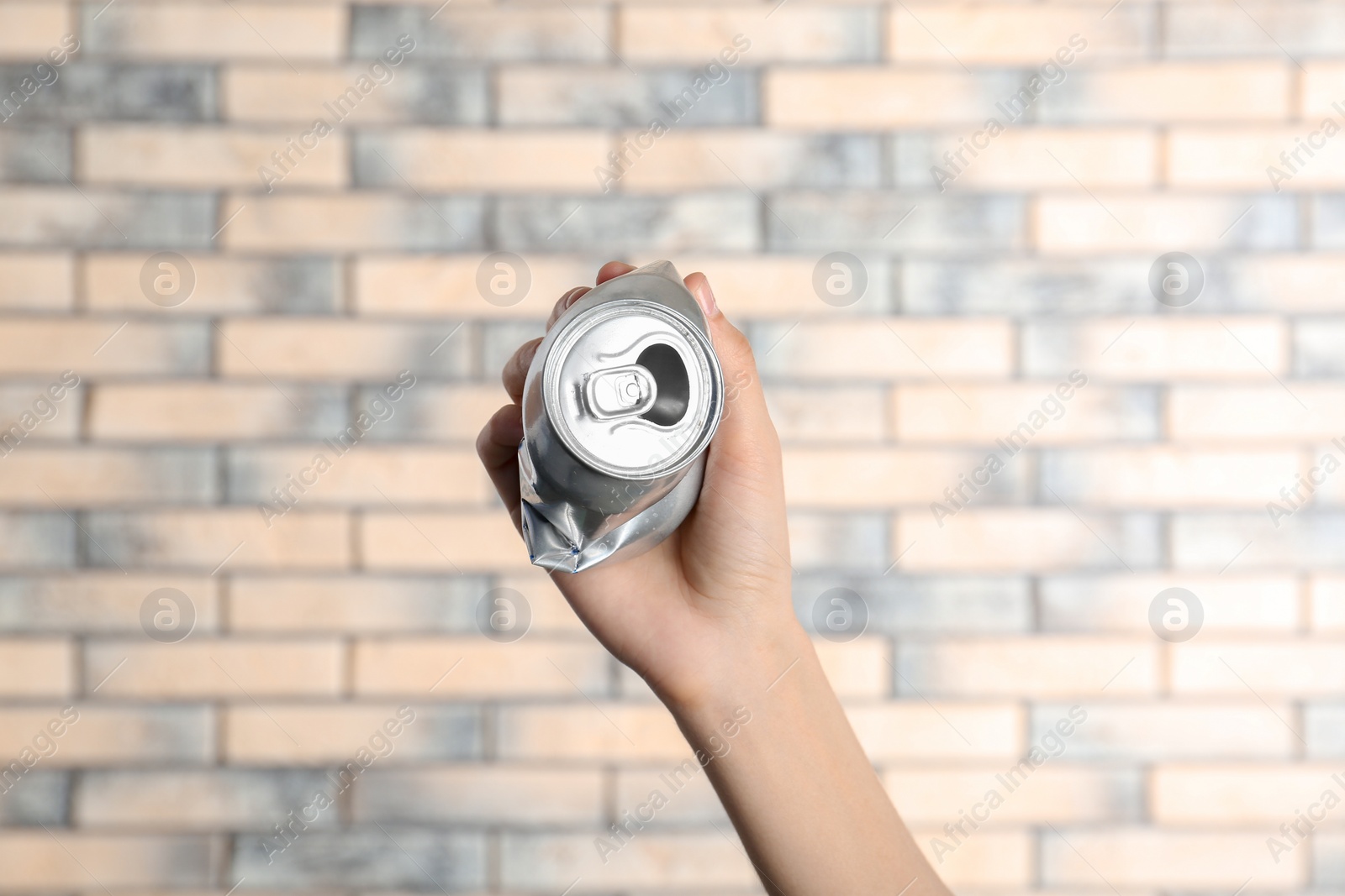 Photo of Woman holding crumpled aluminum can on brick wall background. Metal waste recycling