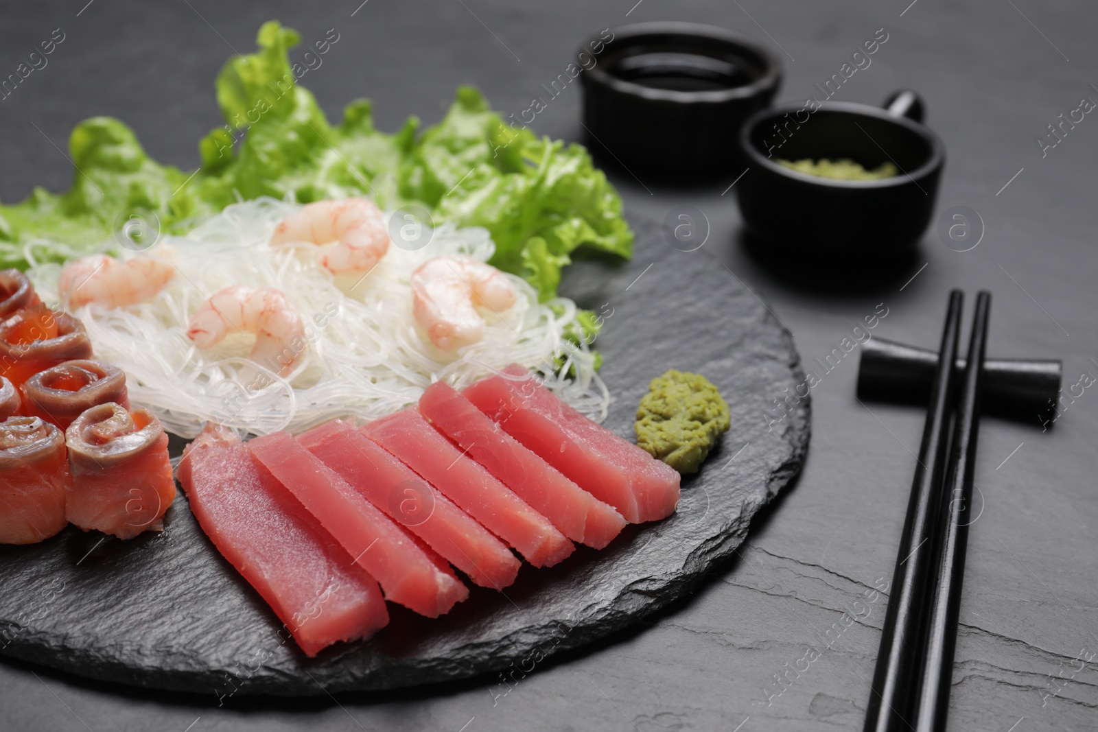 Photo of Sashimi set (raw tuna, salmon slices and shrimps) served with funchosa, lettuce and vasabi on dark table