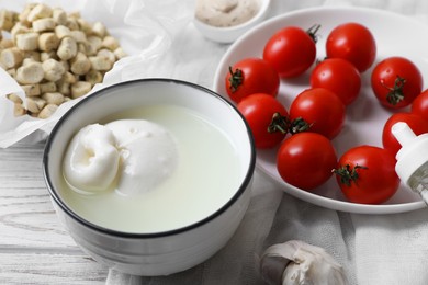 Photo of Delicious burrata cheese served with croutons and tomatoes on white wooden table, closeup