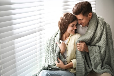 Photo of Happy couple covered with warm green plaid near window indoors