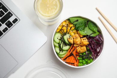 Delicious salad with chicken and vegetables near laptop on white table, flat lay